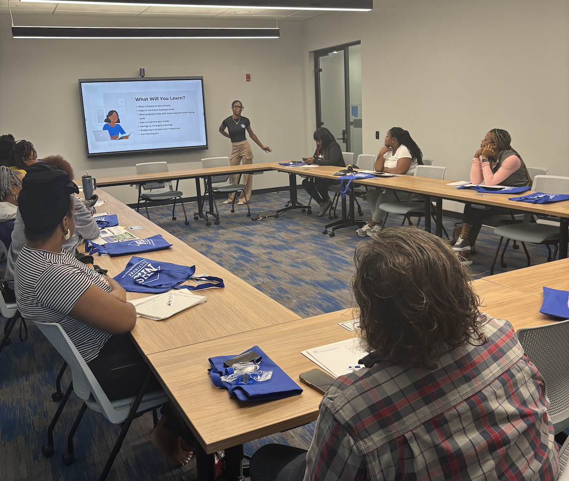 A senior businesswoman gestures as she facilitates a homeowners workshop while working from home. She is talking with the homebuyers workshop participants during a video conference.